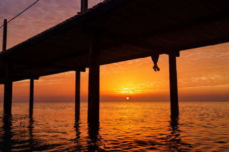 legs of woman who sitting on wooden bridge with beautiful sea landscape at sunrise