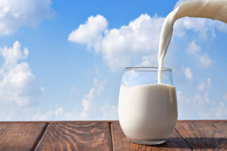 milk pouring from jug into glass on tableの写真素材