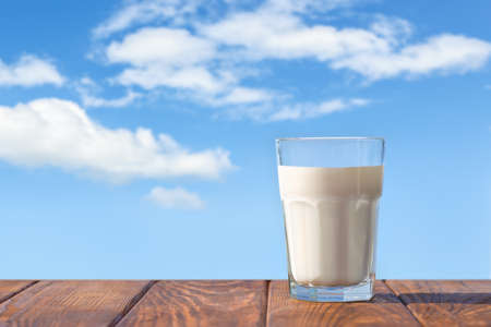 milk in glass on table with blue sky and clouds on the backgroundの写真素材
