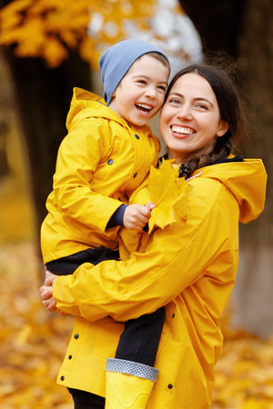 mother in yellow raincoat with son walking and having fun in the autumn parkの写真素材