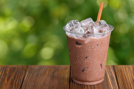 disposable glass of chocolate milkshake with ice on wooden tableの写真素材