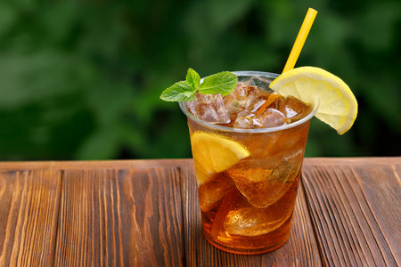 plastic glass with iced tea and lemon on wooden table with green garden on the backgroundの写真素材