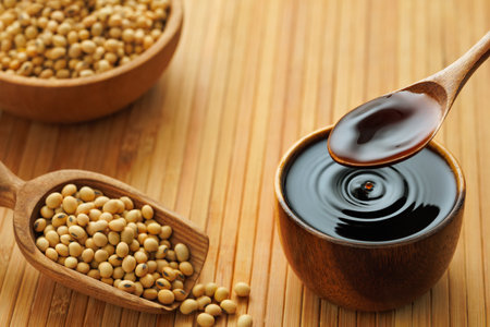 soy sauce pouring in bowl with splash and drop and dry soybeans on wooden tableの写真素材