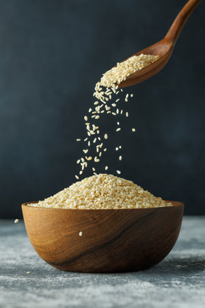 sesame seeds falling from spoon in bowl on tableの写真素材