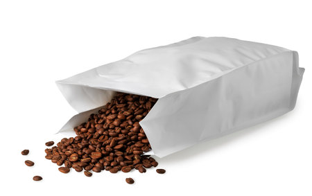 Roasted beans spilling from blank packaging isolated on white background, creating an enticing display for coffee lovers and showcasing product freshnessの写真素材