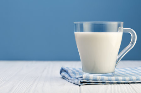 milk in glass cup resting on checkered cloth on white wooden table with blue backgroundの写真素材