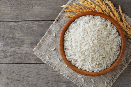 White rice filling wooden bowl on rustic table, complemented by delicate stalksの写真素材