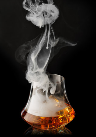Glass of scotch whiskey with ice and cigar smoke on black backgroundの写真素材