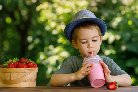 little boy drinking strawberry milkshake or smoothie from disposable plastic glass outdoorsの写真素材