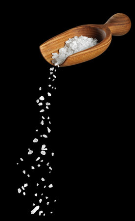 white sea salt falling from wooden scoop isolatedの写真素材