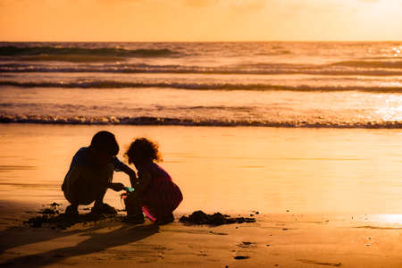Children playing with sand by the sea at sunset in Tobagoの写真素材