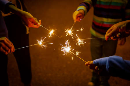 Group hands holding Burning sparking stick starlight fireworks pyrotechnic warm dark background...