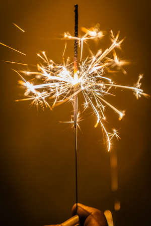 Burning sparking stick starlight fireworks pyrotechnic dark black warm background held on handの写真素材