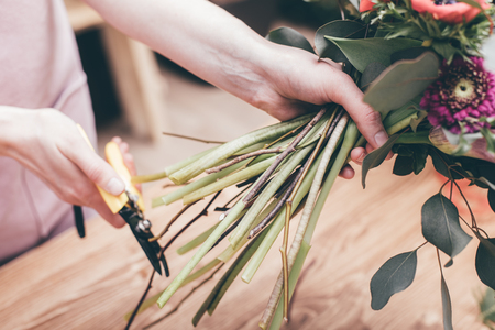 Crop shot of woman cutting stems of green flowers composed in bouquet working in shop.の写真素材