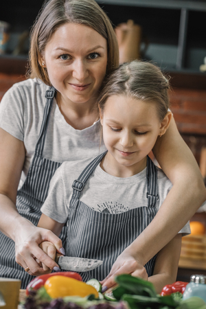 Mother looking at camera and cooking with daughterの写真素材