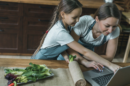 Girl pointing at laptop while cooking with motherの写真素材