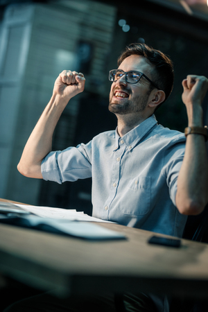 Happy man celebrating win on workplaceの写真素材