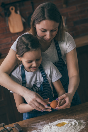 Girl cracking egg to flour with motherの写真素材