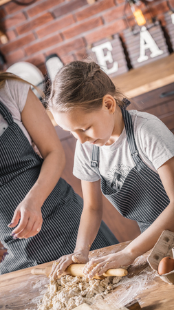 Girl helping mother and rolling doughの写真素材