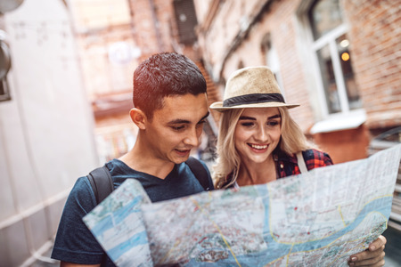 Cheerful casual couple traveling in city and using paper map to create routeの写真素材