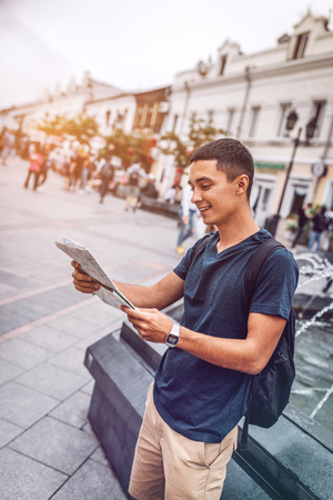 Smiling man exploring map on city streetの写真素材