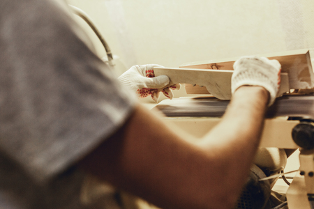 Crop male shaping piece of wood on belt sander