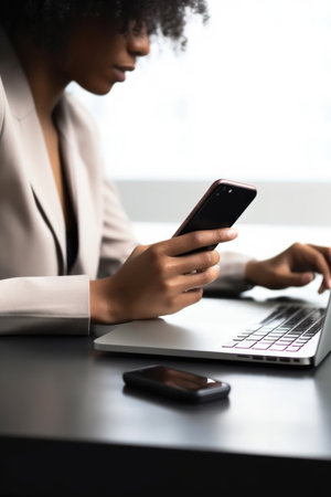 closeup shot of an unidentifiable woman using a cellphone and laptop while sitting at a desk, created with generative aiの素材