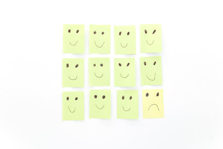 Conceptual image of being sad among happy others. Satisfied, disappointed. Green and yellow sticky notes isolated on white background.の写真素材