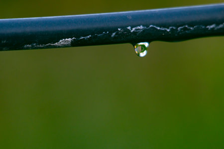 Water drop hanging from a black hoseの写真素材
