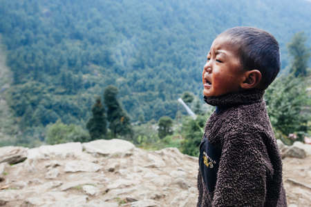 HIMALAYAS, EVEREST REGION, NEPAL - OCTOBER 20, 2018: Portrait nepalese small boy crying near their house, on the street in Himalayan village, Nepalのeditorial素材