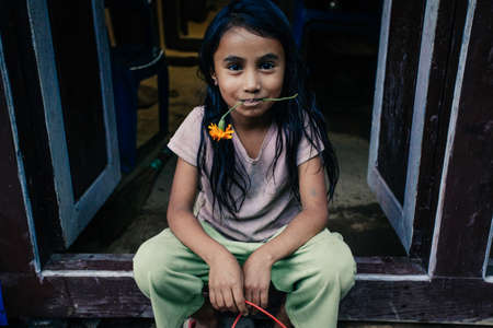 HIMALAYAS, EVEREST REGION, NEPAL - OCTOBER 20, 2010: Portrait nepalese girl near her house, with flower in her mouth, on the street in Himalayan village, Nepalのeditorial素材