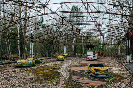Old broken rusty metal radioactive yellow cars, children's electric cars, abandoned among vegetation, the park of culture and recreation in the city of Pripyat, the Chernobyl disaster, Ukraine.の写真素材