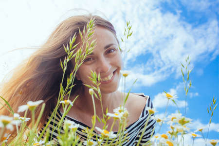 Beautiful young woman with brown hait, smiling, in chamomile field