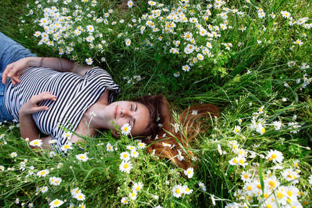 Beautiful young woman with brown hait, smiling, in chamomile fieldの写真素材