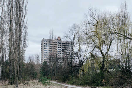 Dilapidated building with the USSR coat of arms on the roof. Abandoned building in ghost town Pripyat. Abandoned city overgrown with trees.のeditorial素材
