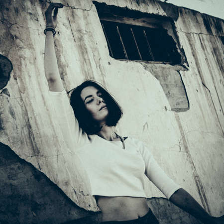 Lonely woman leaning against concrete wall in urban environment.の写真素材