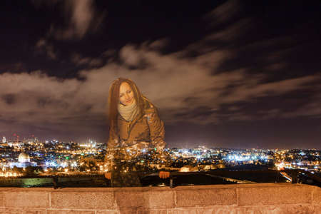 Young woman sitting on background of Jerusalem at night with the Al-Aqsa Mosque and the Mount of Olivesの写真素材