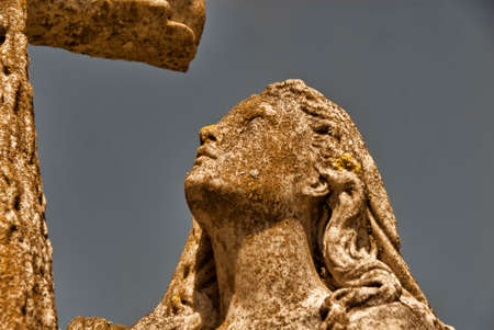 A statue of a woman gazing up at a cross.の写真素材