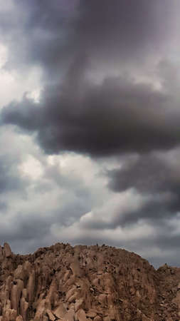 Stormy rain clouds over a mountain of rocks.の写真素材