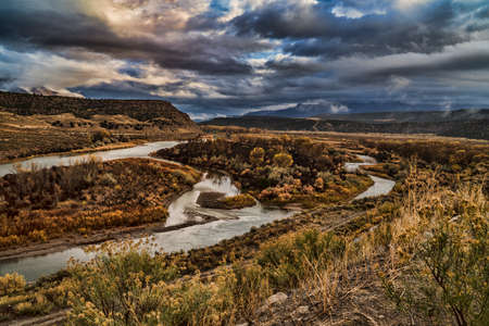 The Colorado River fows through fall colors under stormy skies.の写真素材