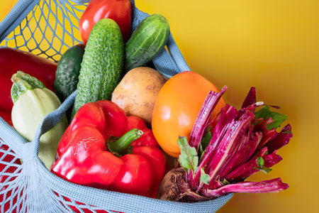 Close-up part of mesh shopping bag full of fresh farm vegetables on yellow backgroundの写真素材