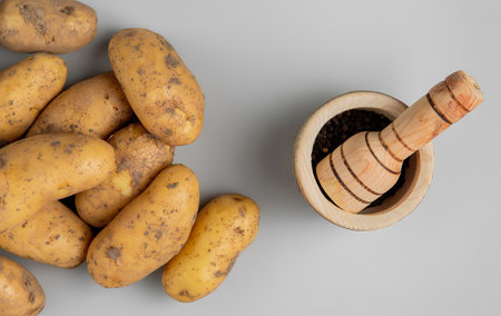 top view of potatoes in basket plate and black pepper seeds in garlic crusherの写真素材
