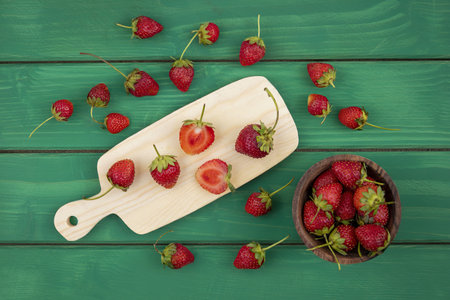 top view of slices of strawberry on a wooden kitchen board with strawberries on a wooden bowl