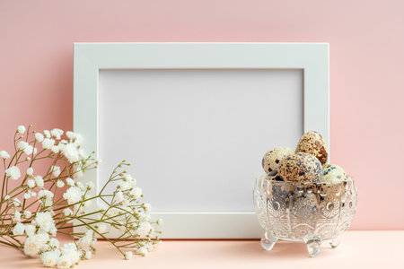 Empty white frame, quail eggs in crystal bowl and white gypsophila on pastel pinkの写真素材