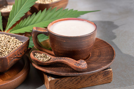 Hemp milk in ceramic cup and grains in brown ceramic bowl and spoon and cannabis leavesの写真素材