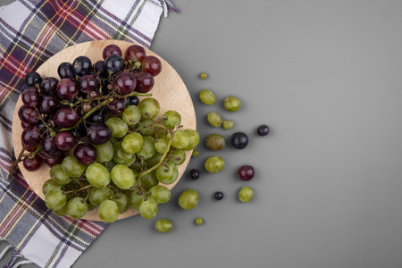 top view of grapes on cutting board on plaid cloth with grape berries on gray background with copy spaceの写真素材