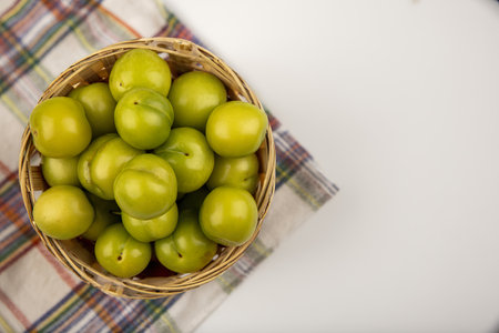 top view of green plums in basket on plaid cloth on white background with copy spaceの写真素材