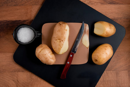 top view of potatoes salt knife on cutting board on wooden backgroundの写真素材