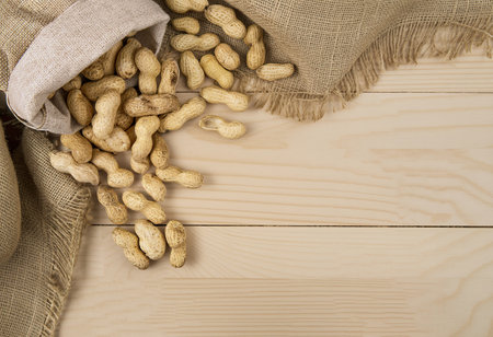 top view of peanuts in shell scattered from a sack on wooden background with copy space