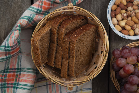 top view of rye bread slices in basket on plaid cloth with bowl of nuts and basket of grapesの写真素材